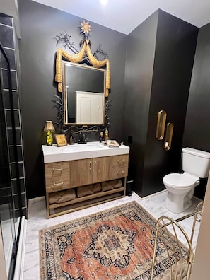 Un bany amb una paret fosca, un lavabo blanc amb marc daurat, un mirall gran i un vàter.