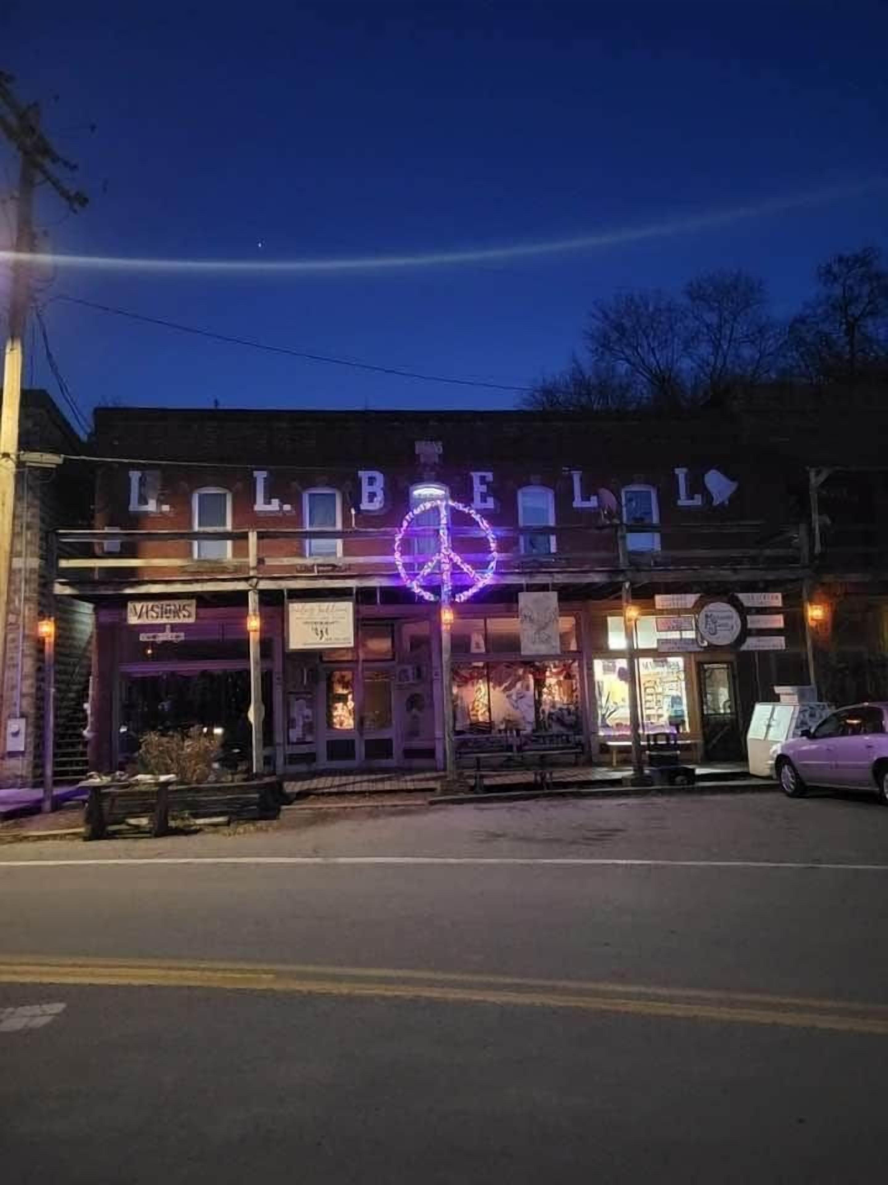 A building with a neon sign, a storefront, and a parked car.