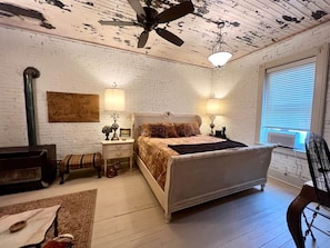 Ein Schlafzimmer mit einem Bett, zwei Nachttischen, einem Deckenventilator, einem Fenster mit Jalousien und einer Ziegelwand.