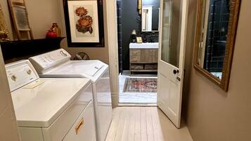 A laundry room with a washing machine and dryer, a framed picture on the wall, and a mirror on the right.