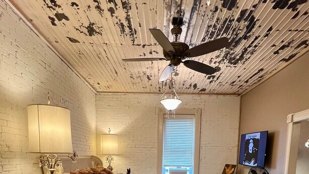 A bedroom with a bed, a desk, a chair, a television, and a ceiling fan. - Vulture's Roost (Makanda)