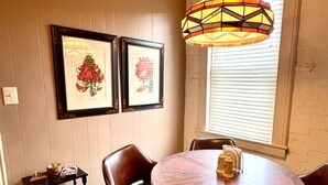 A dining area with a round table, four chairs, a pendant light, and two framed artworks on the wall. - Vulture's Roost (Makanda)