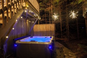 A hot tub with a wooden deck and string lights, surrounded by a wooden fence and trees. - Quietside Tree House - Peaceful 1-bedroom studio with AC in Acadia Mount Desert (Mount Desert)