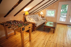 A cozy room with a wooden floor, a sofa, a table, and a foosball table. - Quietside Tree House - Peaceful 1-bedroom studio with AC in Acadia Mount Desert (Mount Desert)