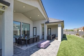 Eine überdachte Terrasse mit Esstisch und Stühlen, eine kleine Sitzecke und ein gepflegter Rasen.