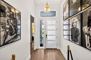 A hallway with framed black and white photographs on the walls, a white door with frosted glass panels, and a potted plant in the doorway. - Red Rock Retreat - 4BR - Hot Tub - Fire Pit (Hurricane)