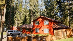 Une cabane en bois rouge à deux étages, dotée d’une cour clôturée et entourée de grands arbres.