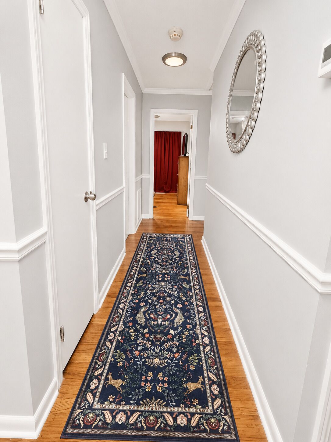A hallway with white walls, a wooden floor, and a dark blue patterned rug.