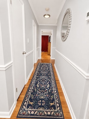 A hallway with white walls, a wooden floor, and a dark blue patterned rug. - Pet-friendly 3-bedroom house in Florence, AL two mile from UNA! (Florence)
