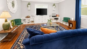 Una sala de estar con un sofá azul, un televisor de pantalla plana, una mesa de centro y una alfombra estampada.