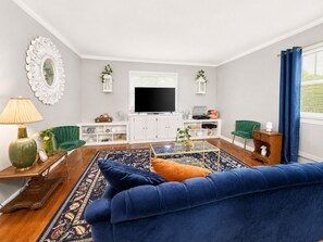 Ein Wohnzimmer mit einem blauen Sofa, einem Flachbildfernseher, einem Couchtisch und einem gemusterten Teppich.