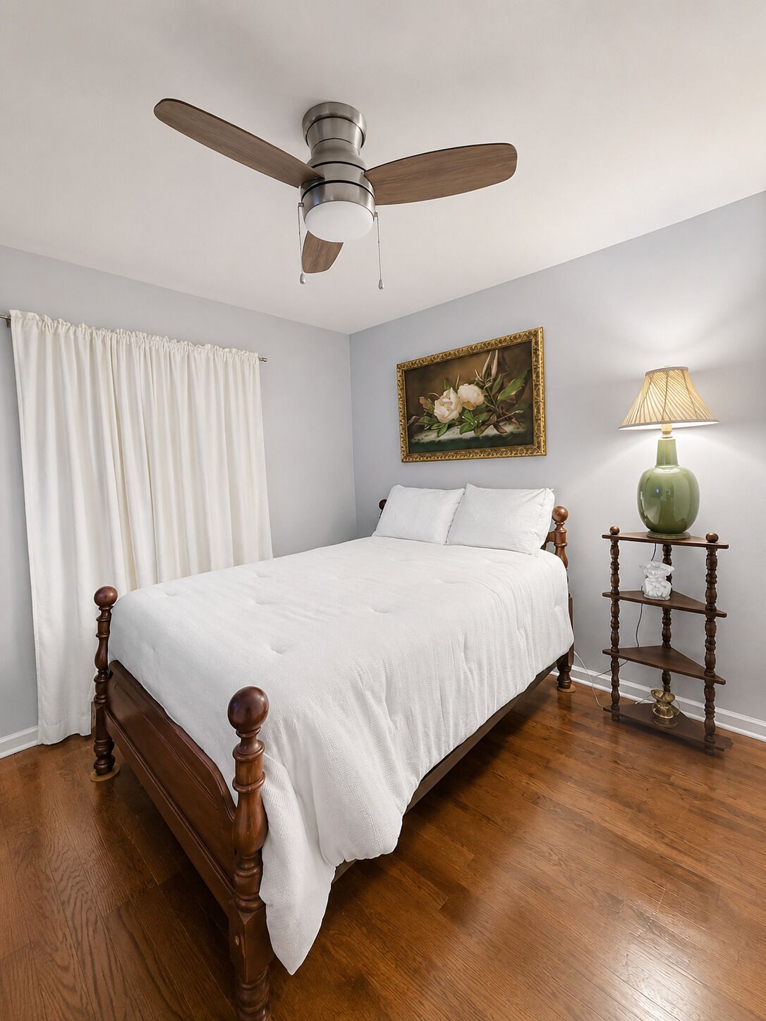 Une chambre à coucher avec un lit en bois, un ventilateur de plafond, un tableau et une lampe sur une table de chevet.