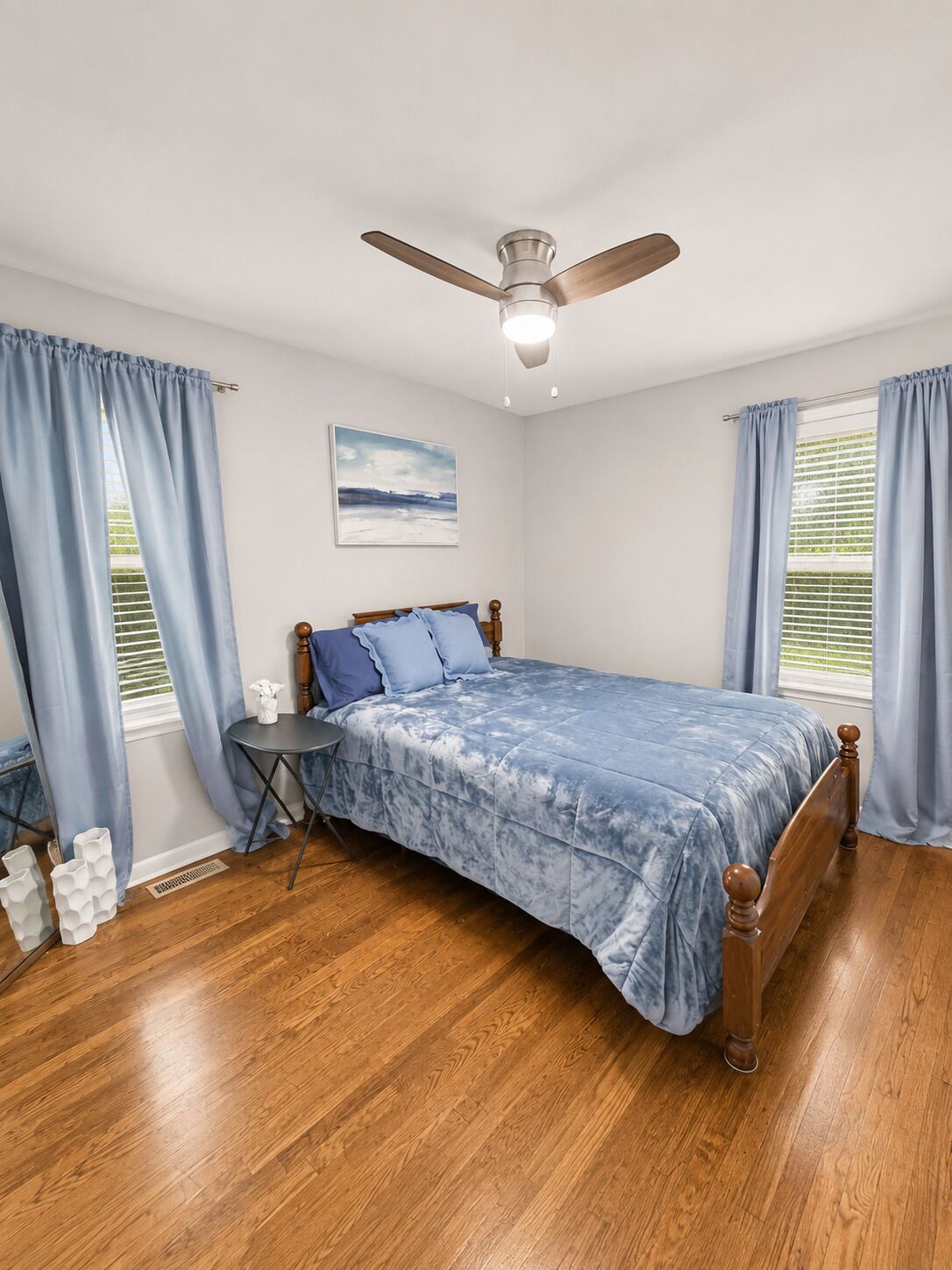 A bedroom with a bed, a ceiling fan, a window with blinds, and a painting on the wall.