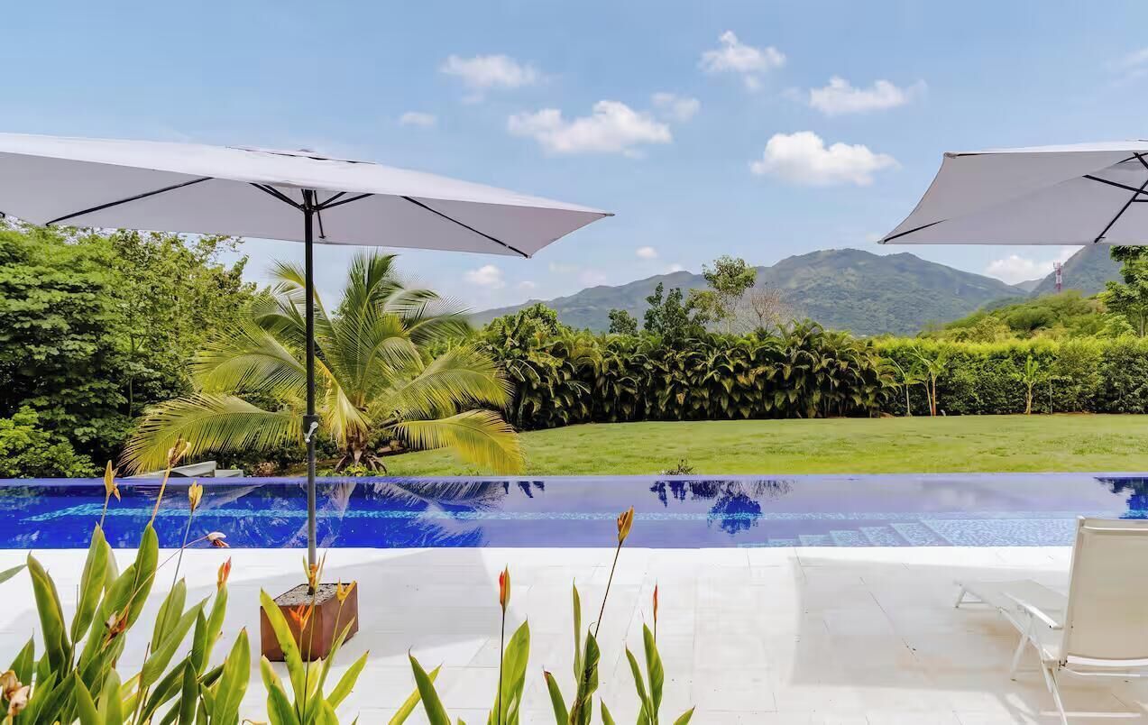 A swimming pool with two umbrellas, surrounded by lush greenery and a view of mountains.