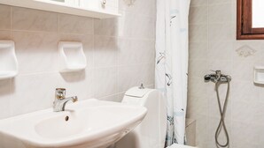 Une salle de bain avec un lavabo blanc, des toilettes, une douche avec un rideau et un miroir au-dessus du lavabo.