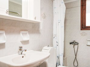 A bathroom with a white sink, a toilet, a shower with a curtain, and a mirror above the sink. - Apartment 7 with seaview and beautiful sunset by Interhome (Chania)