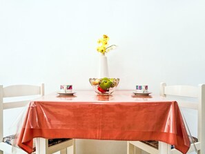 A table with a red tablecloth, two white chairs, a white vase with yellow flowers, and two cups with saucers.