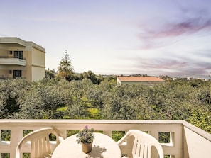 A terrace with a table and chairs, overlooking a densely vegetated area with buildings in the background.