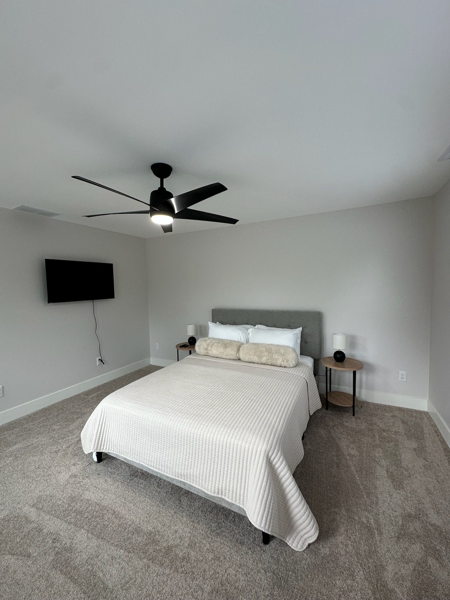 A bedroom with a bed, a ceiling fan, a wall-mounted TV, and bedside tables.