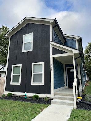 A two-story house with a dark exterior, white trim, and a covered porch. - New Modern 4-bedroom 3-Bath Home near downtown Indianapolis and Speedway (Indianapolis)