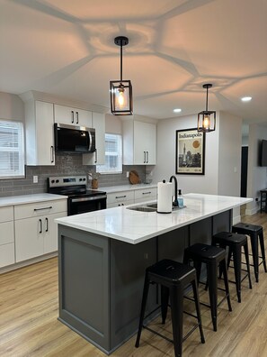 A modern kitchen with a large island, stainless steel appliances, and bar stools. - New Modern 4-bedroom 3-Bath Home near downtown Indianapolis and Speedway (Indianapolis)