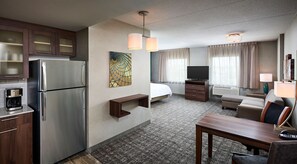 A hotel room with a kitchenette, a bed, a seating area, and a television.