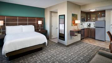 A hotel room with a bed, bedside lamps, a small desk, a mirror, a kitchenette, and a bathroom.