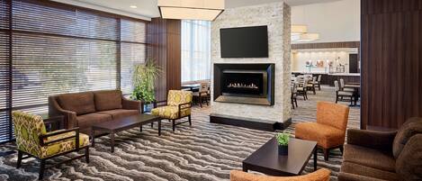A hotel lobby with a fireplace, seating area, and a view of the dining area.