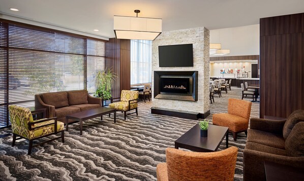 A hotel lobby with a fireplace, seating area, and a view of the dining area.