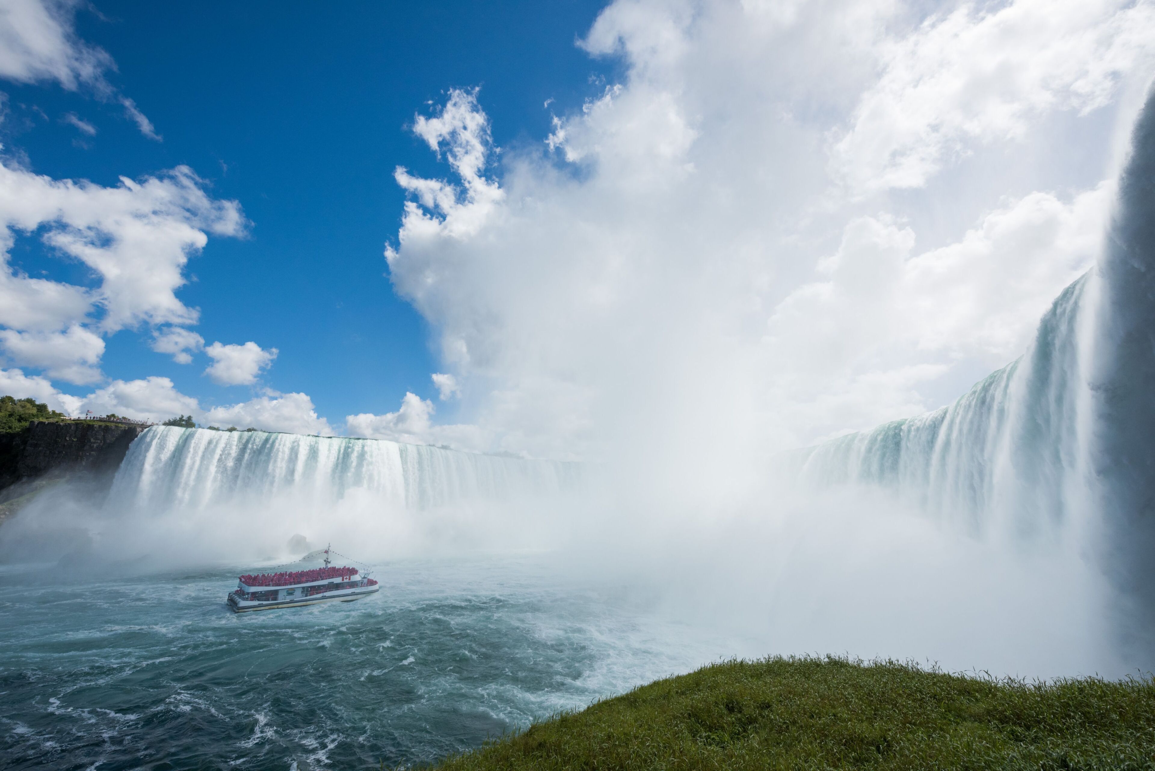 A boat navigating through a large waterfall with a clear sky above.