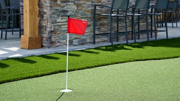 Un campo da golf con una bandiera rossa su un manto erboso, un muro in pietra e un'area relax all'aperto.