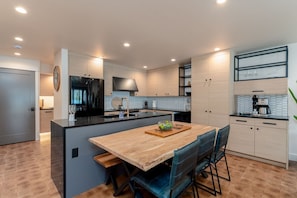 A modern kitchen with a central island, built-in appliances, and a dining area with chairs. - Yacine Court (Manson)