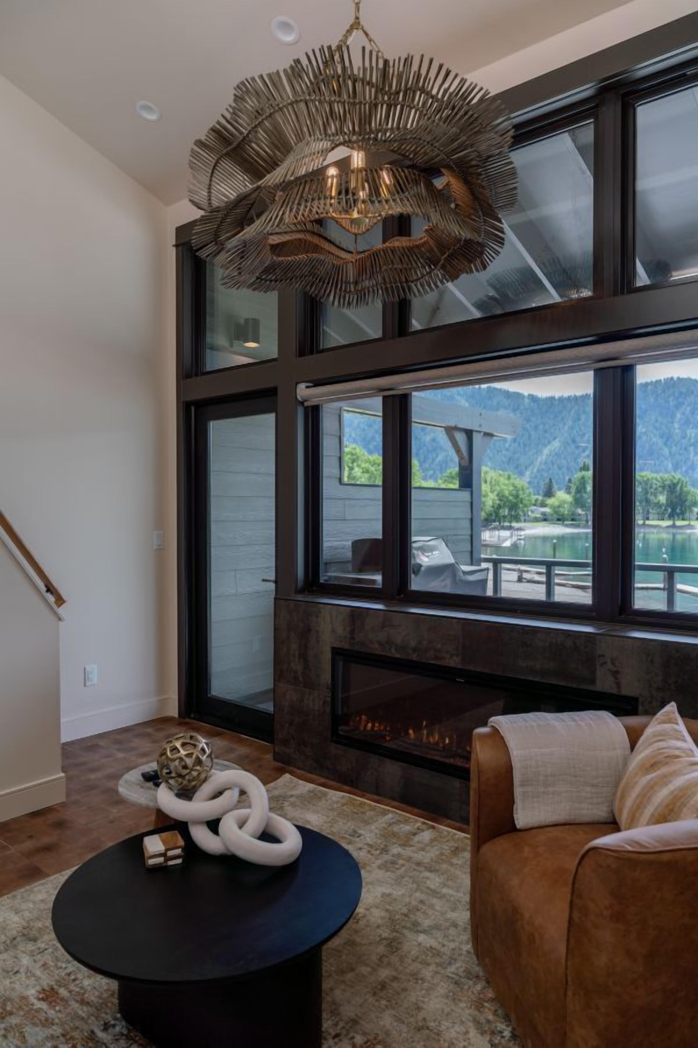 A modern living room with a fireplace, large windows, and a view of a lake and mountains.