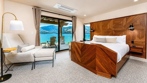 Un dormitorio con una cama, una silla, una lámpara y vistas a un lago.