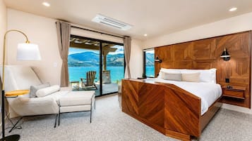 A bedroom with a bed, a chair, a lamp, and a view of a lake.