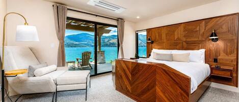 A bedroom with a bed, a chair, a lamp, and a view of a lake.
