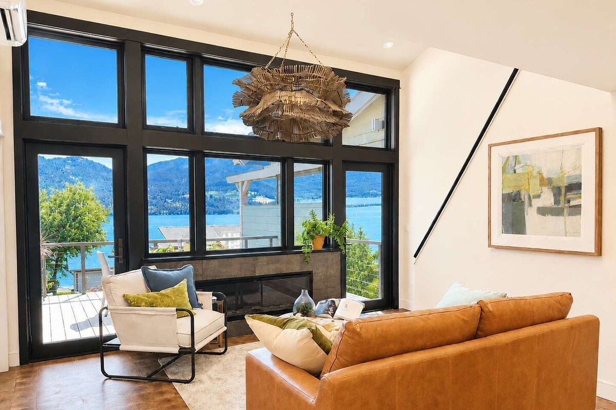 A modern living room with a large window, a fireplace, a sofa, and a hanging light fixture.