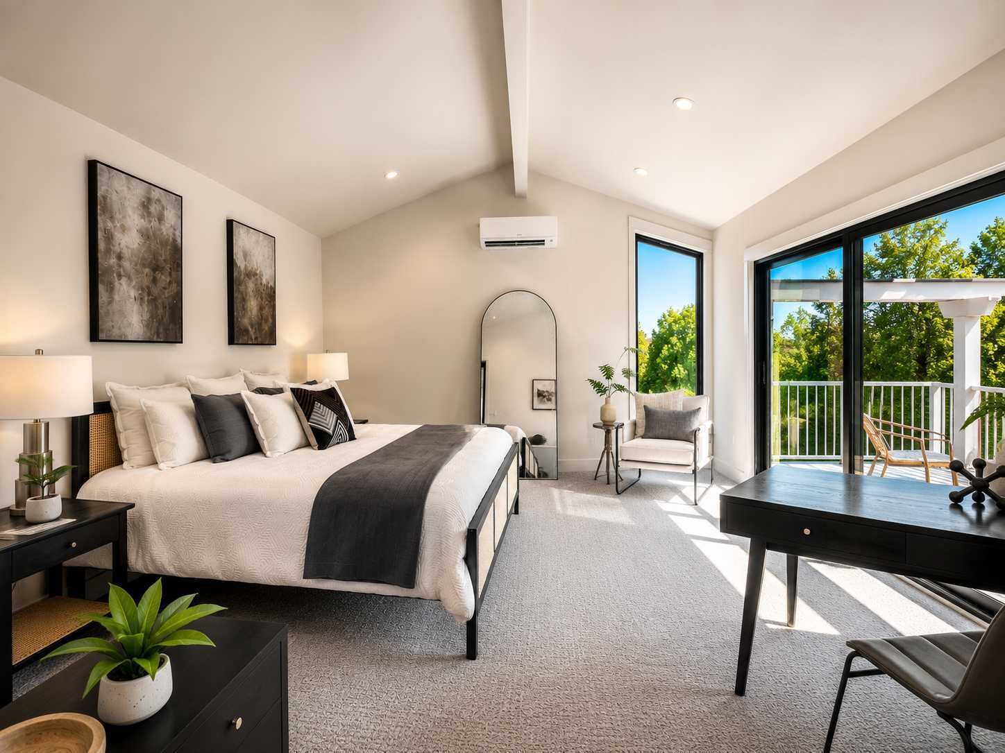 A modern bedroom with a large bed, bedside tables, a desk, and a balcony with outdoor seating.