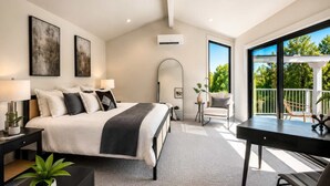 Un dormitorio moderno con una cama grande, mesitas de noche, un escritorio y un balcón con mobiliario exterior.