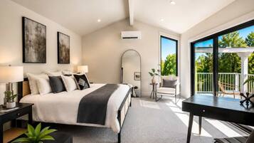 A modern bedroom with a large bed, bedside tables, a desk, and a balcony with outdoor seating.