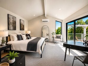 A modern bedroom with a large bed, bedside tables, a desk, and a balcony with outdoor seating. - Yacine Court (Manson)