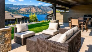 Un patio exterior con mobiliario de mimbre y vistas a montañas y un lago.