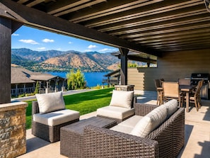 An outdoor patio with wicker furniture and a view of mountains and a lake. - Yacine Court (Manson)