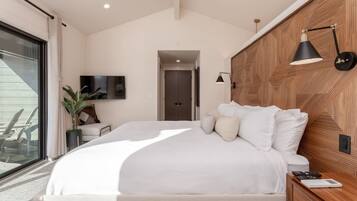 Een moderne slaapkamer met een groot bed, een houten hoofdbord, een nachtkastje, een aan de muur bevestigde televisie en uitzicht op het groen via een schuifdeur.
