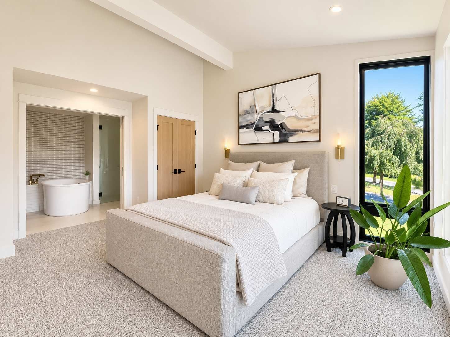 A bedroom with a large bed, a walk-in closet, a bathtub, and a view of trees through a window.