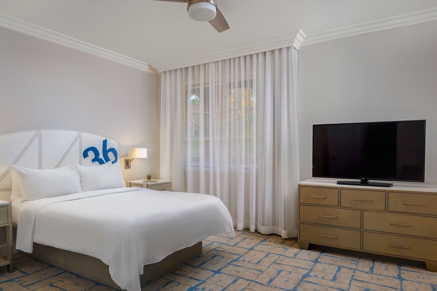 Une chambre d’hôtel avec un lit, une télévision, une table de chevet, une lampe et une fenêtre avec des rideaux.