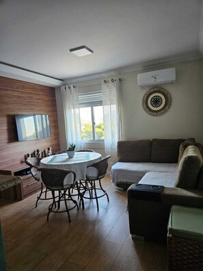 A living room with a round table, chairs, a sofa, a television, and a wall-mounted air conditioner. - Apartment on the beachfront next to the Aquarium. (Balneário Camboriú)
