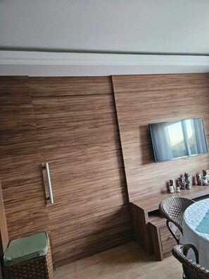 A modern room with a built-in TV, a wooden panel wall, a wicker chair, and a small table. - Apartment on the beachfront next to the Aquarium. (Balneário Camboriú)
