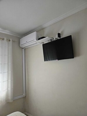 A room with a mounted air conditioner, a television, and a window with a curtain. - Apartment on the beachfront next to the Aquarium. (Balneário Camboriú)