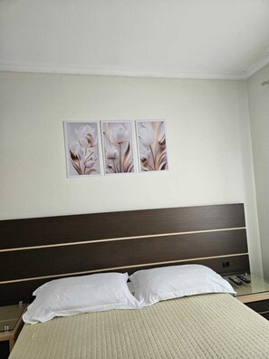 A hotel room with a bed, white pillows, a headboard, and three wall-mounted pictures of flowers. - Apartment on the beachfront next to the Aquarium. (Balneário Camboriú)